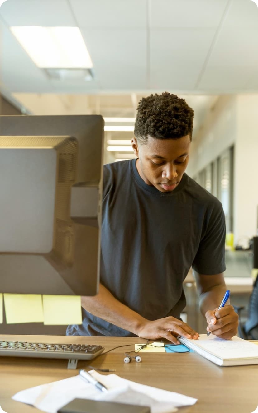 man with computer writing on a note